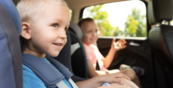 The image shows two young children sitting in the backseat of a car, secured in their car seats.