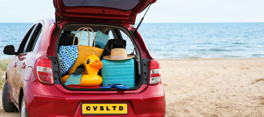 This image shows the open trunk of a red car parked on a sandy beach with the sea in the background, suggesting a sunny day.